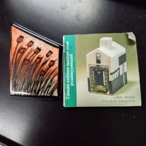 Arabian Heljä Liukko-Sundströmin suunnittelema rintakoru, jossa on oranssisävyinen kukka-aihe sekä mukana alkuperäinen pakkaus ja tuotekortti.