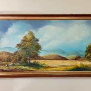 Pitkänomainen kehystetty maisemamaalaus, jossa etualalla on suuri puu, taustalla kumpuilevia kukkuloita ja sinertäviä vuoria pilvisen taivaan alla.