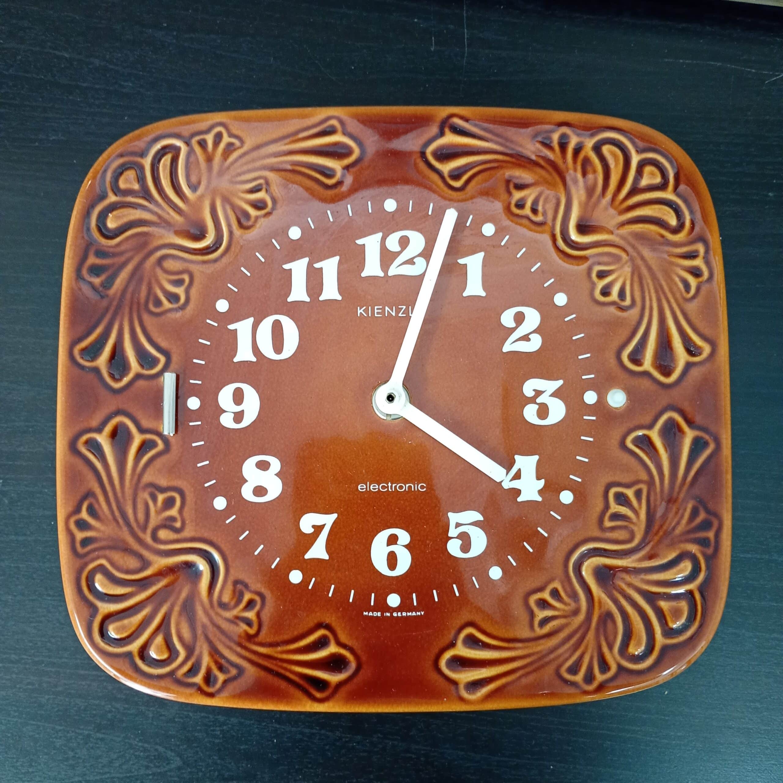 Ruskea vintage Kienzle seinäkello, jossa koristeellinen keramiikkakehys ja valkoinen kellotaulu