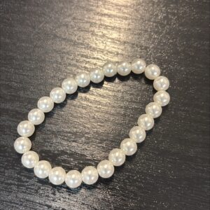 Elastinen helmirannekoru suurilla vaaleilla helmillä mustaa taustaa vasten.