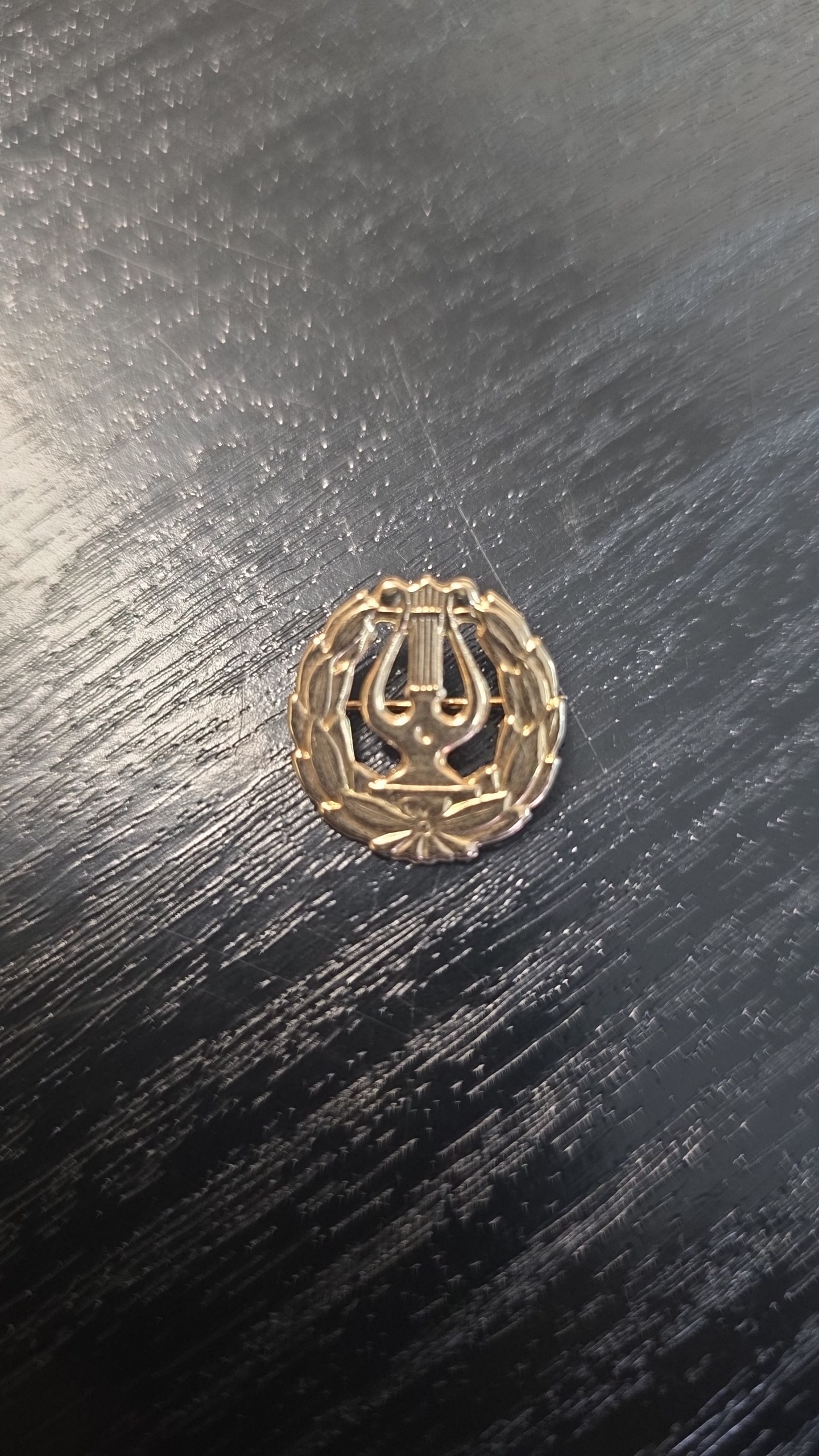 925 hopeinen lyyra-rintaneula mustaa puupintaa vasten.