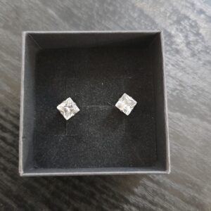 Hopeiset princess cut -korvanapit värittömillä kivillä mustalla korualustalla.