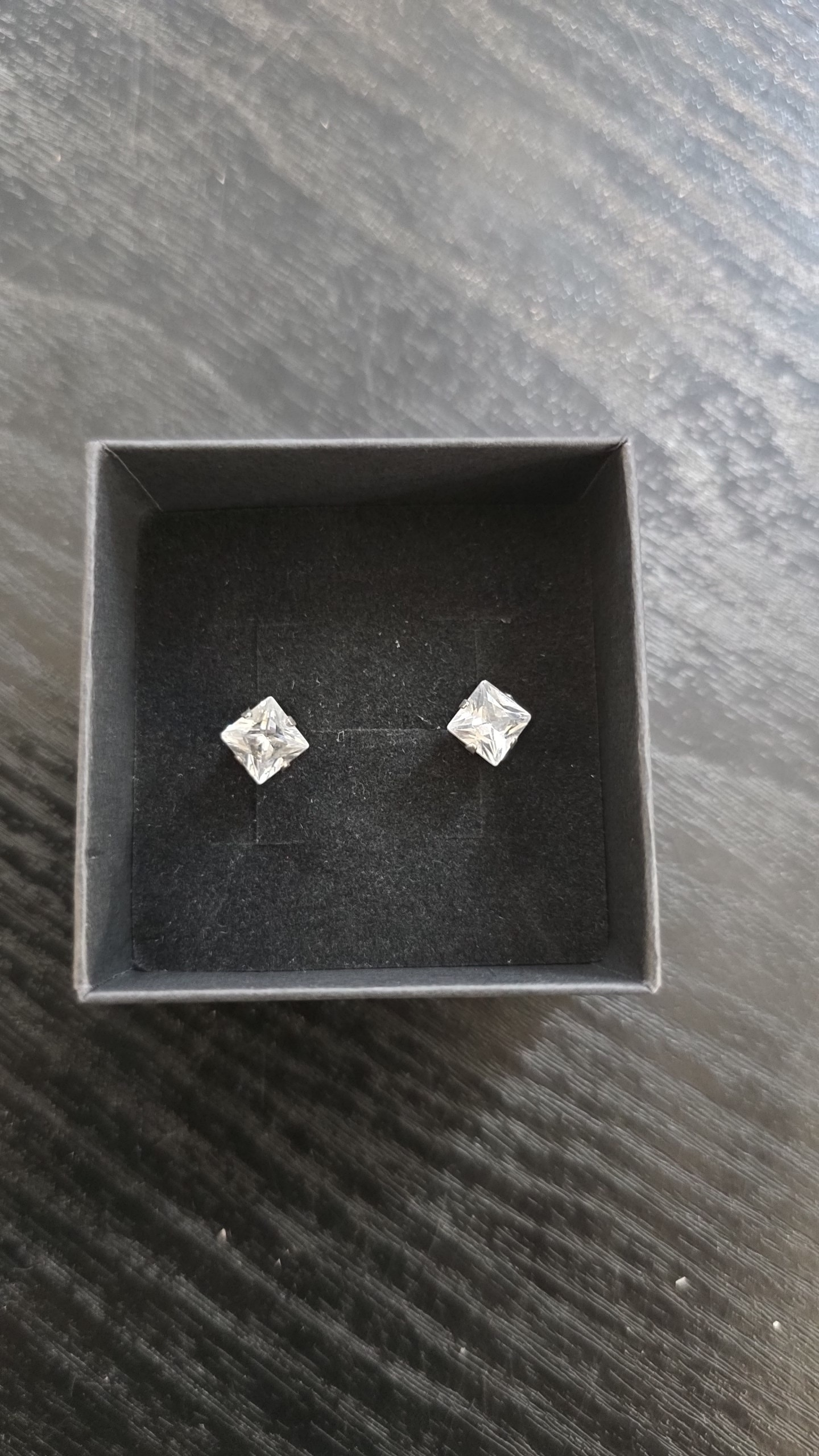Hopeiset princess cut -korvanapit värittömillä kivillä mustalla korualustalla.