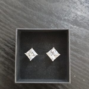 Hopeiset princess cut -kivikorvakorut värittömillä kivillä mustalla korualustalla.